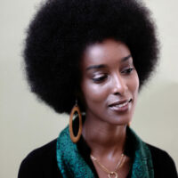 Ladan Osman in a black top with a green scarf, large earrings and a necklace