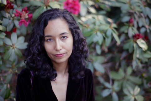 Safia Jama stands outside in front of a flowering bush, looking at the camera