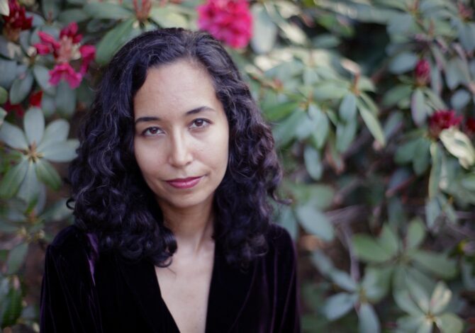 Safia Jama stands outside in front of a flowering bush, looking at the camera