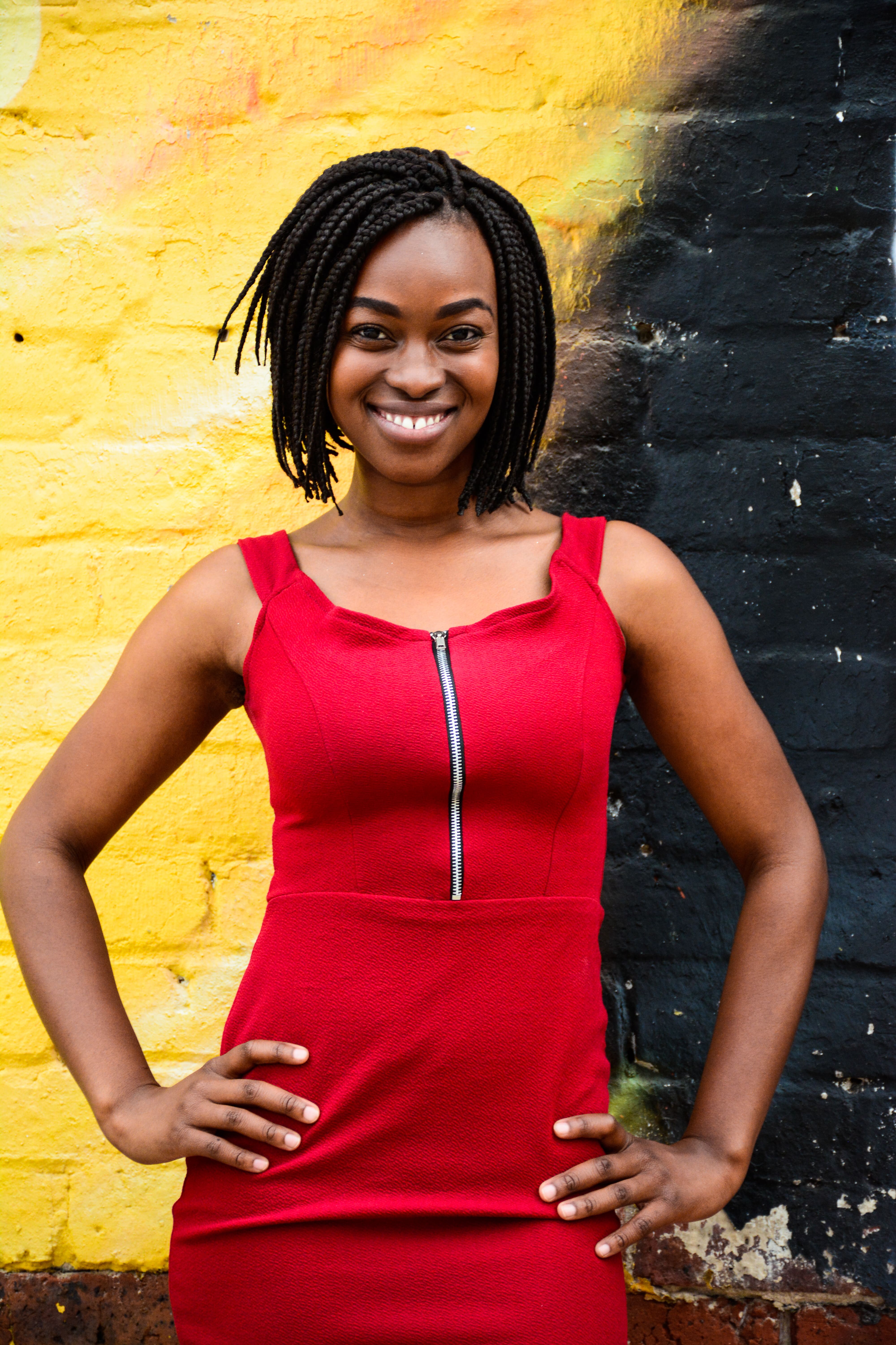 Nkateko Masinga stands in sunlight in front of a brick wall wearing a red dress
